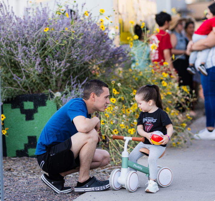 man crouched speaking to young girl on tricycle in garden
