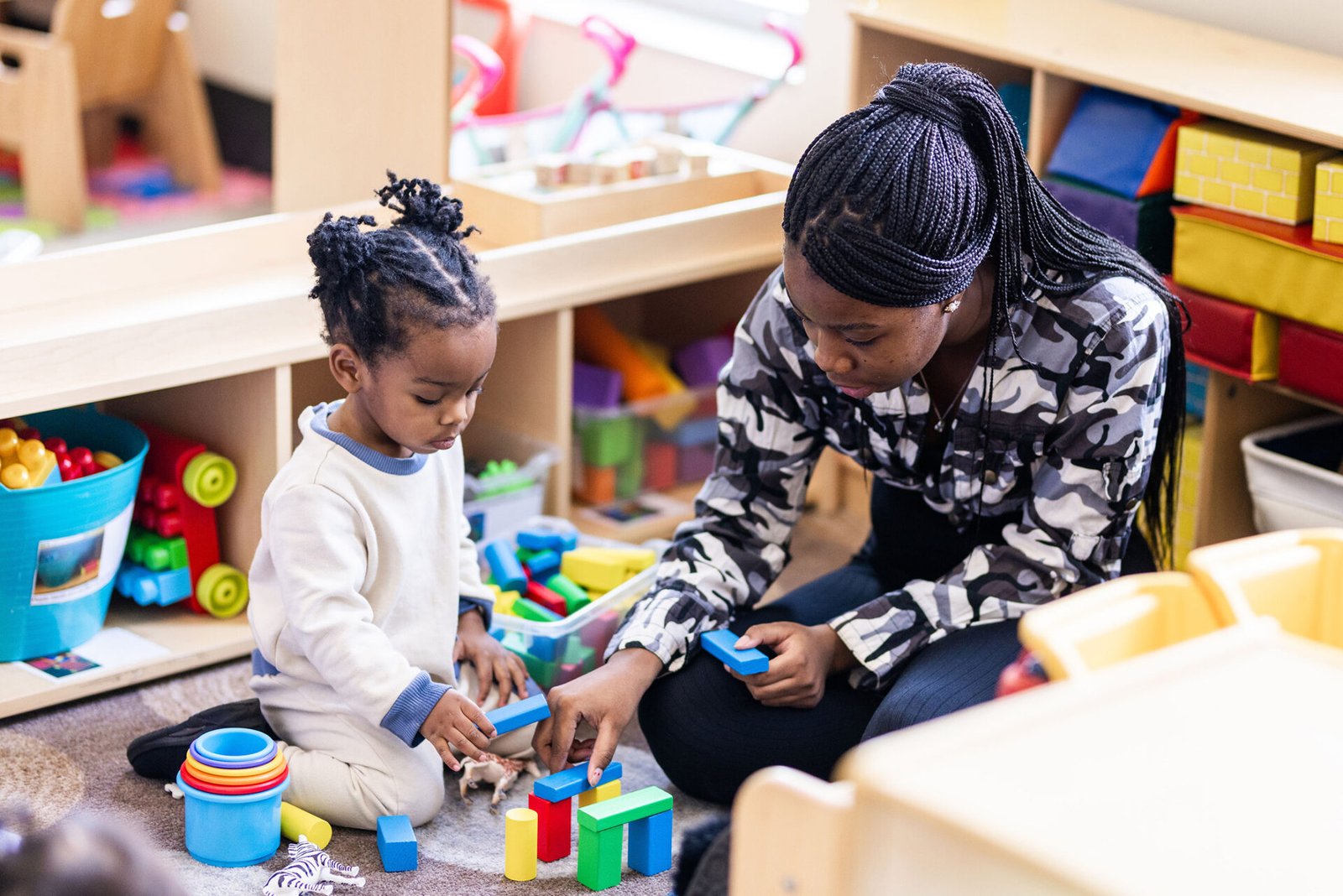 a woman shows a young girl building blocks in a classroom
