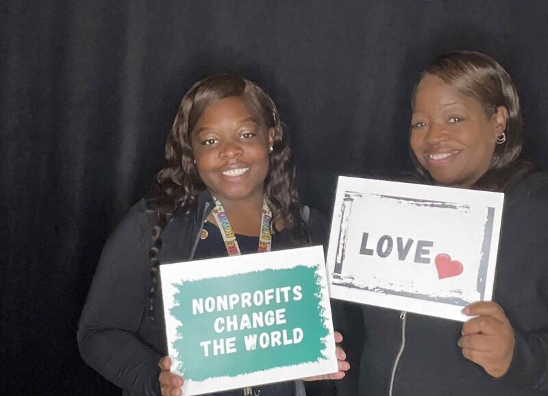 two women smiling with signs that say "nonprofits change the world" and "love"